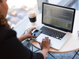 Person working on a Mac while reaching for their phone