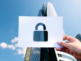 Hand holding a paper with a lock shaped hole in the middle on a skyscraper background.